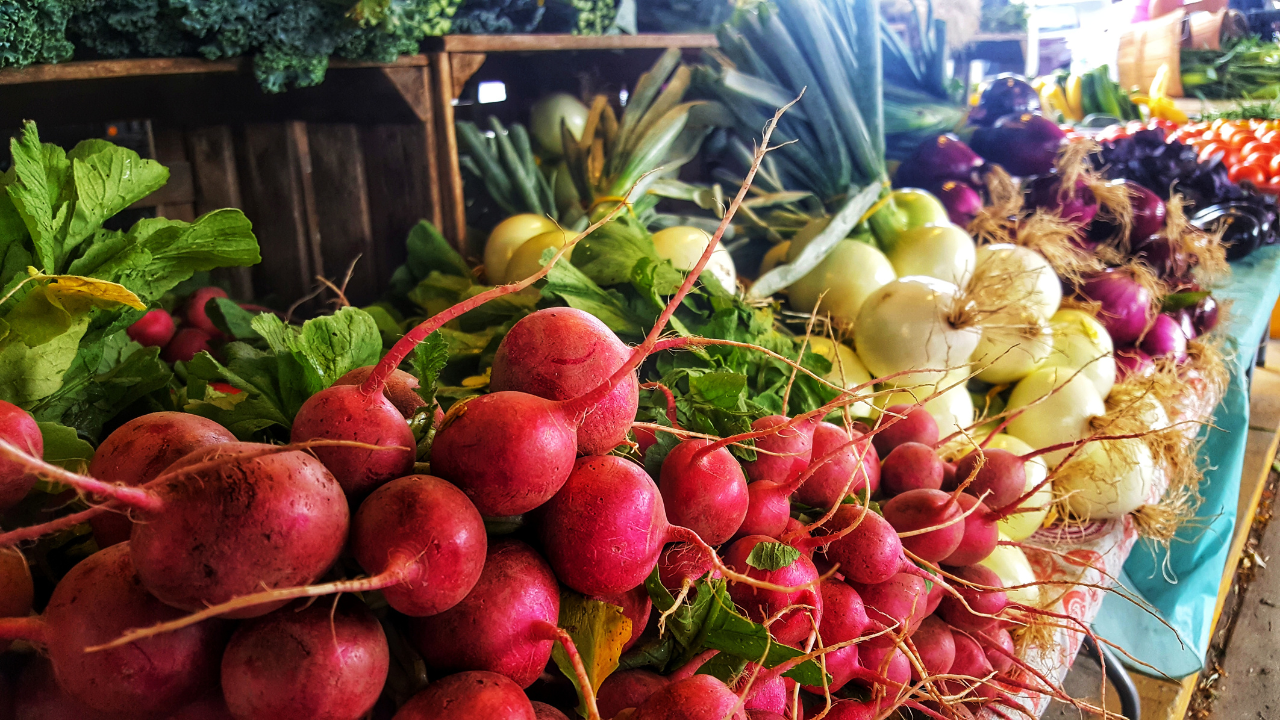 A farmer's market stall piled with fresh radishes and vegetables
